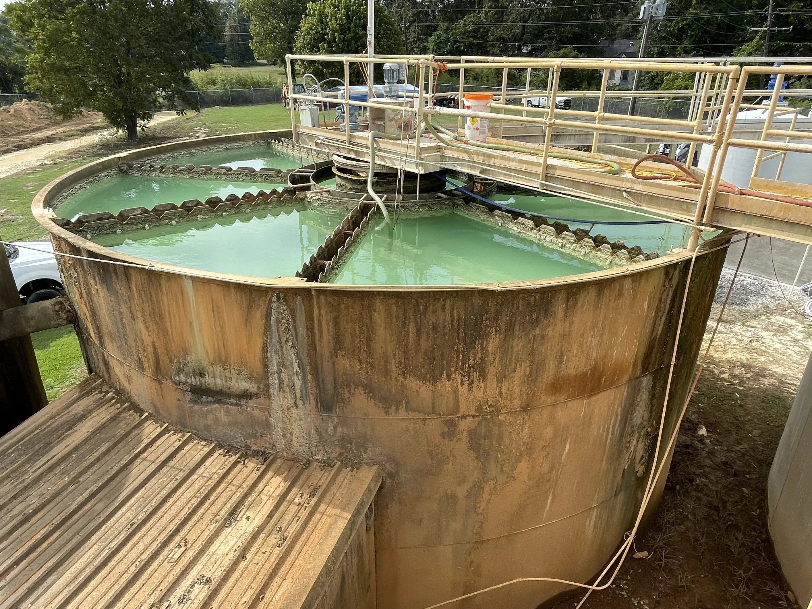 A round clarifier tank with green-tinted water and a steel walkway at a small water treatment plant