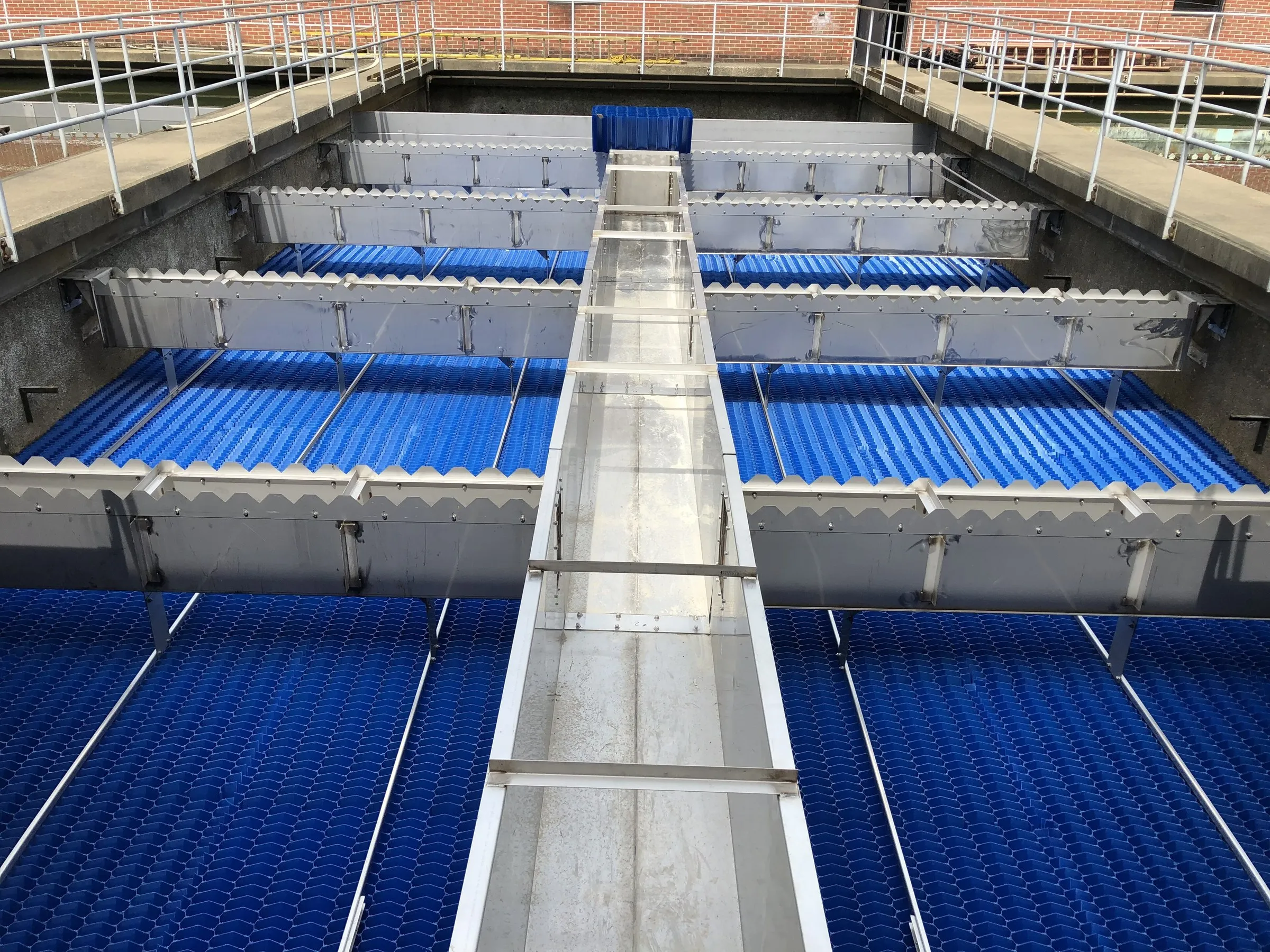Blue lamella plates inside a settling tank at a water treatment plant, with a steel walkway down the middle