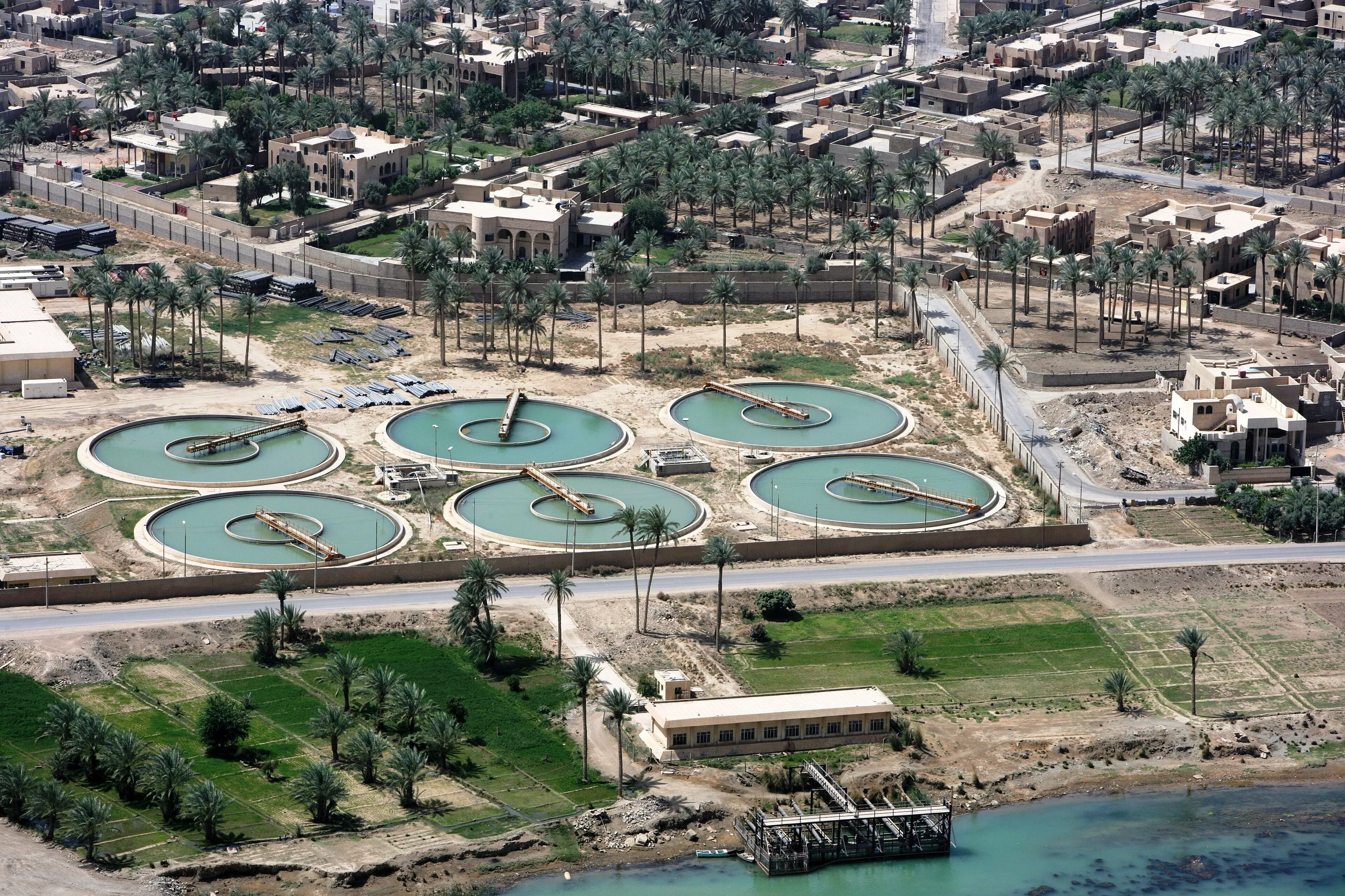 An aerial view of round settling tanks at a water treatment plant beside a river