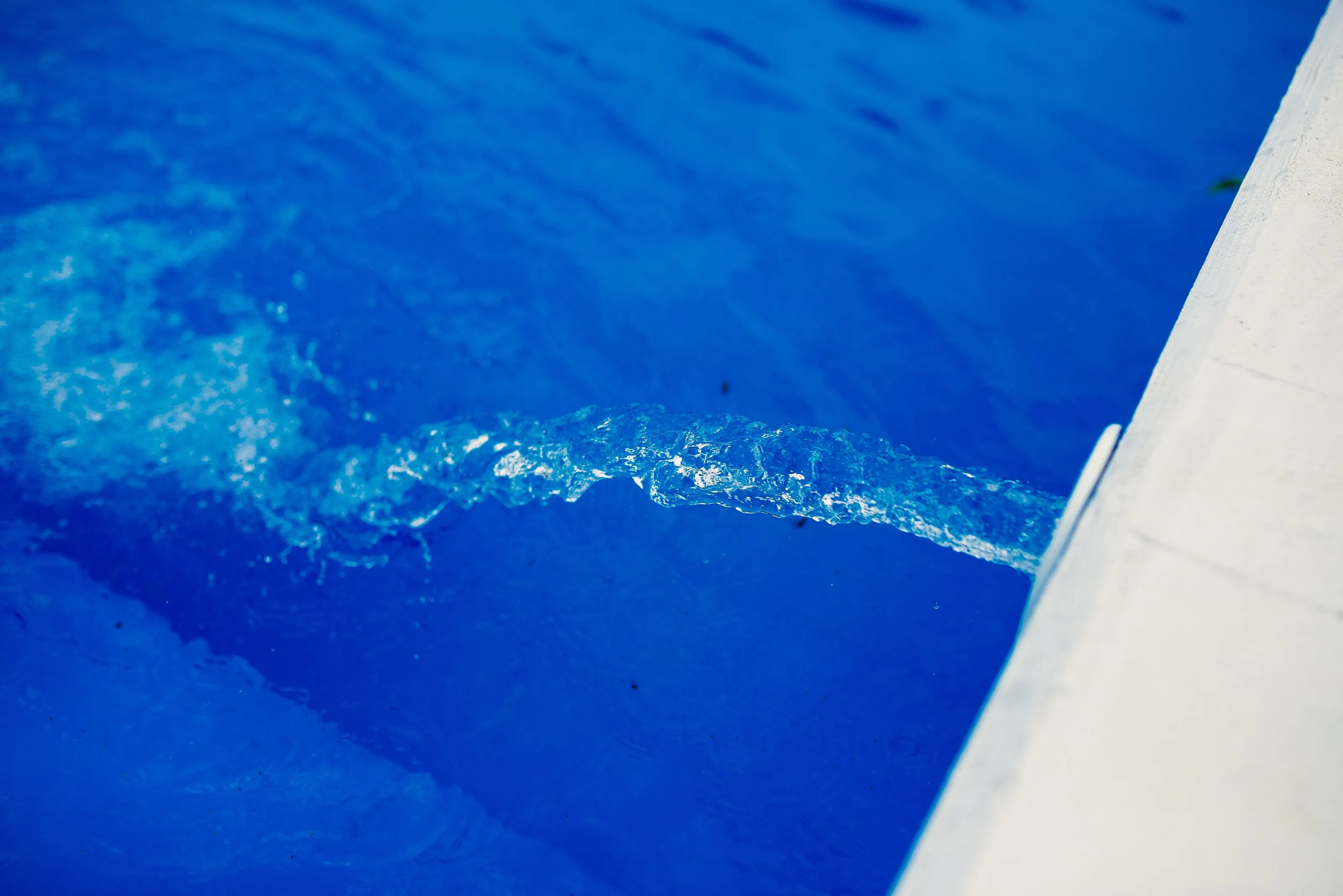 Water flowing from an inlet into a bright blue swimming pool
