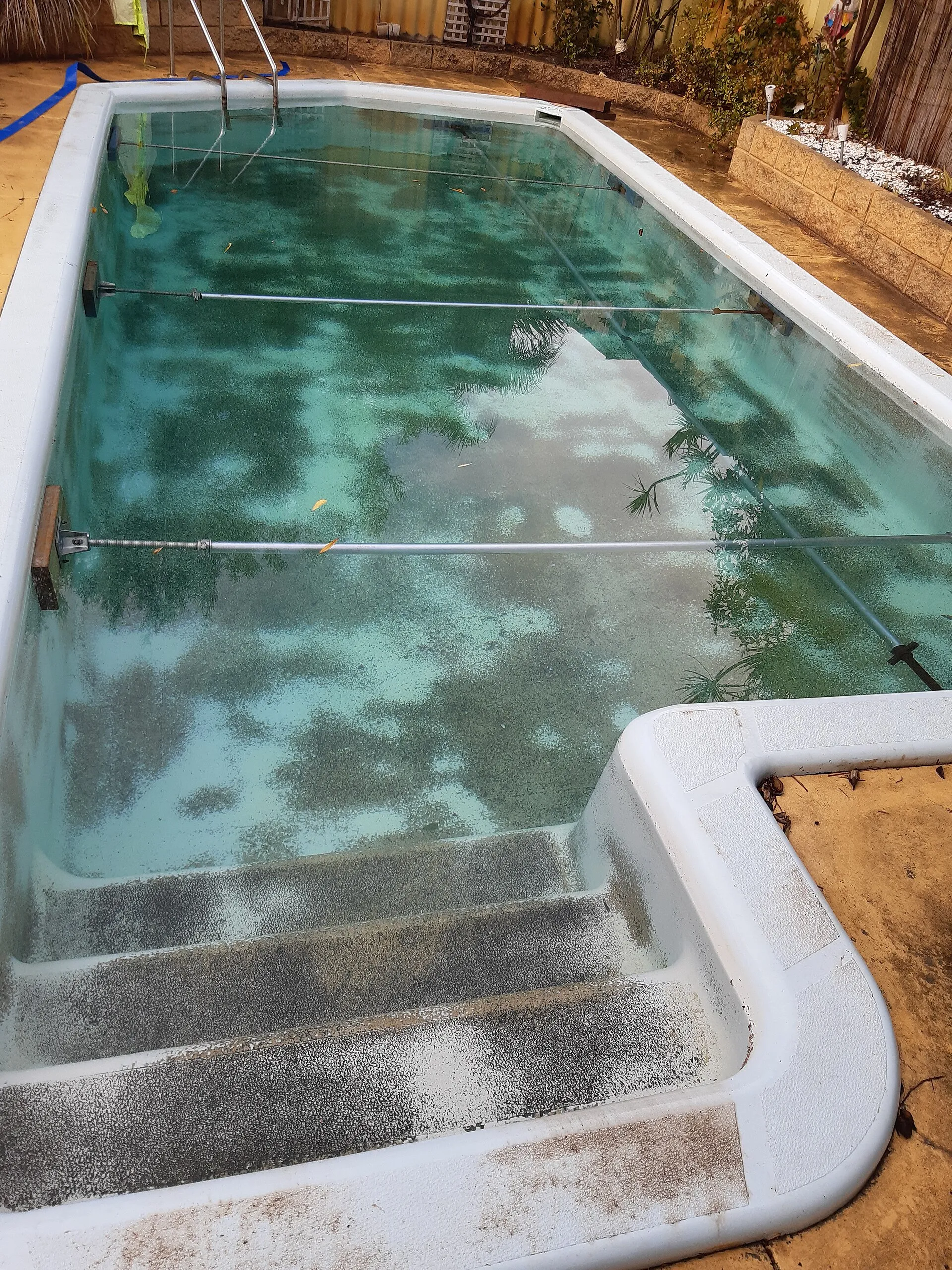 A swimming pool being cleaned, with a pole across the clear green water