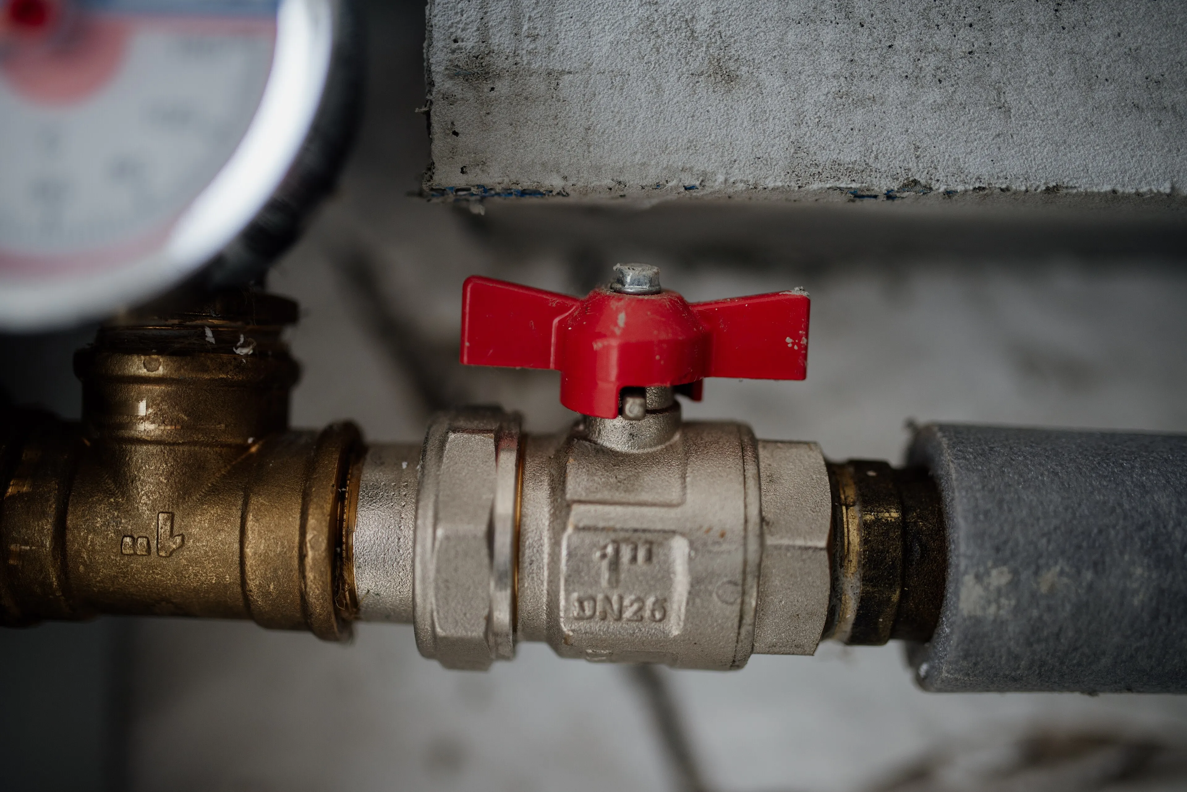 A red-handled ball valve on a metal water pipe with a pressure gauge above it